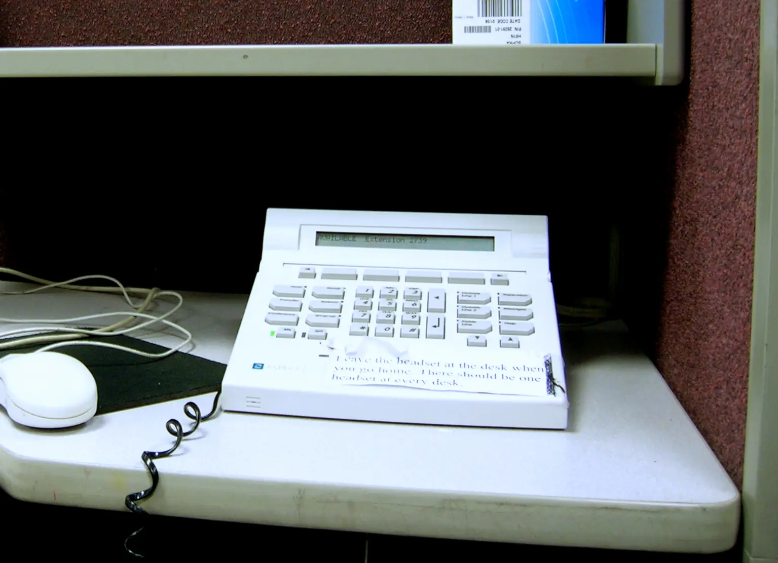 A call-centre desk telephone console and mouse on a cubicle shelf