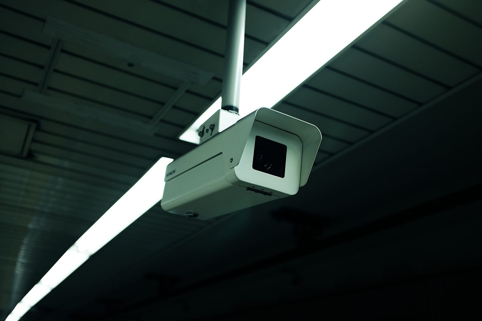 A CCTV surveillance camera mounted on a ceiling next to strip lights