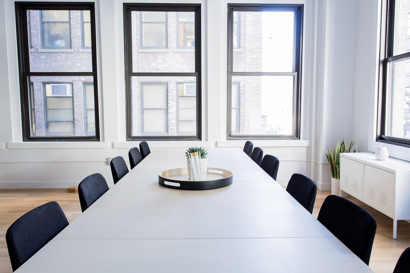 An empty, bright meeting room with a long white table and black chairs