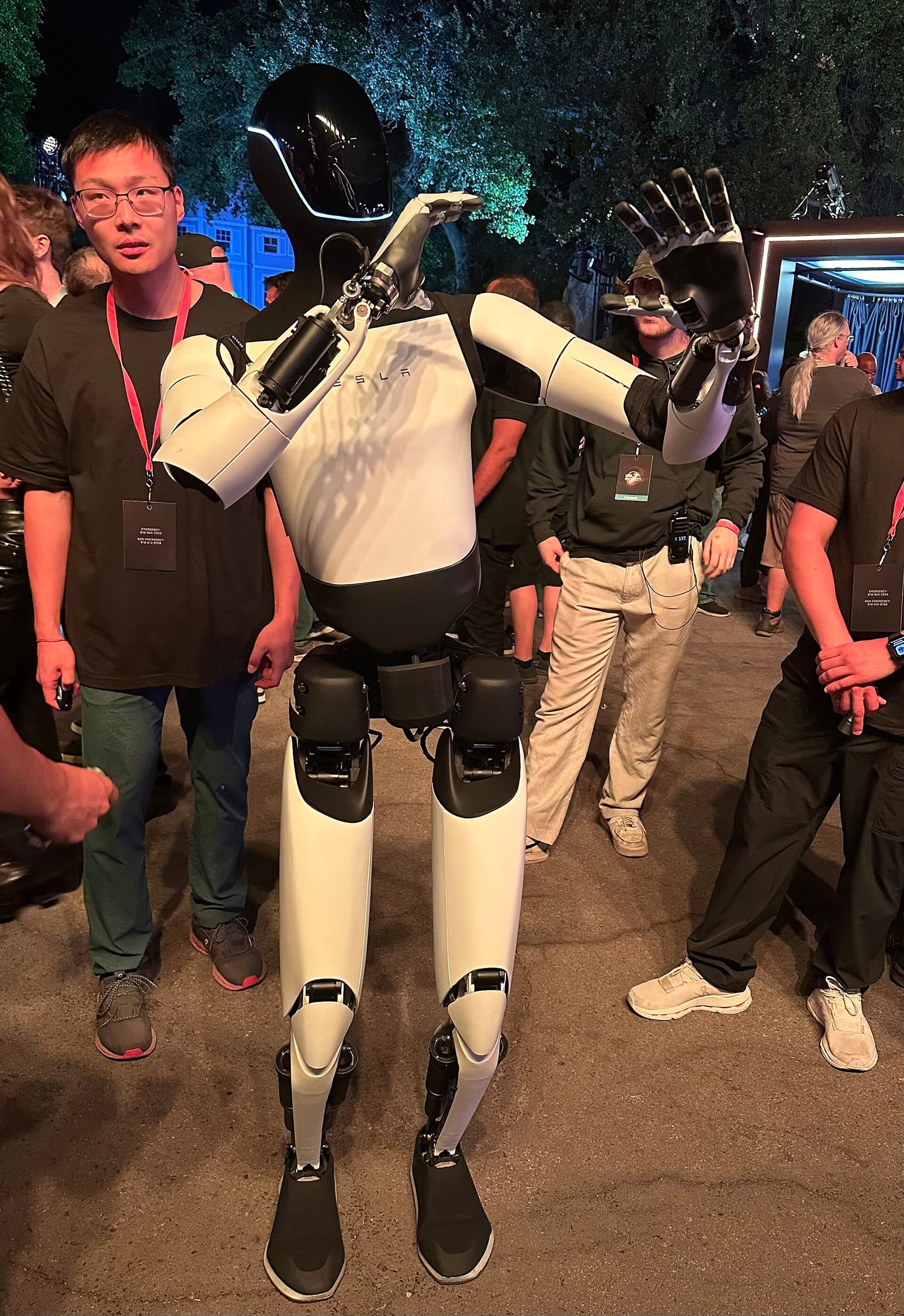 A Tesla Optimus humanoid robot standing among visitors at an event