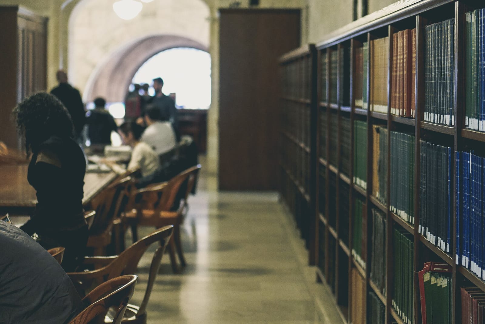Library reading room with long rows of bookshelves and people studying at tables
