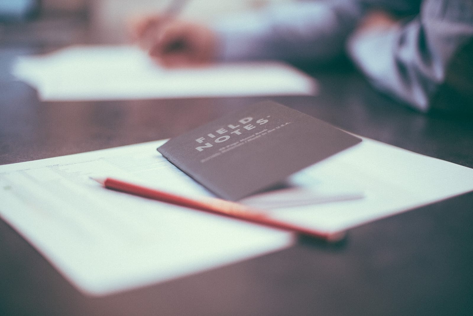Small notebook and a pencil lying on sheets of paper on a desk